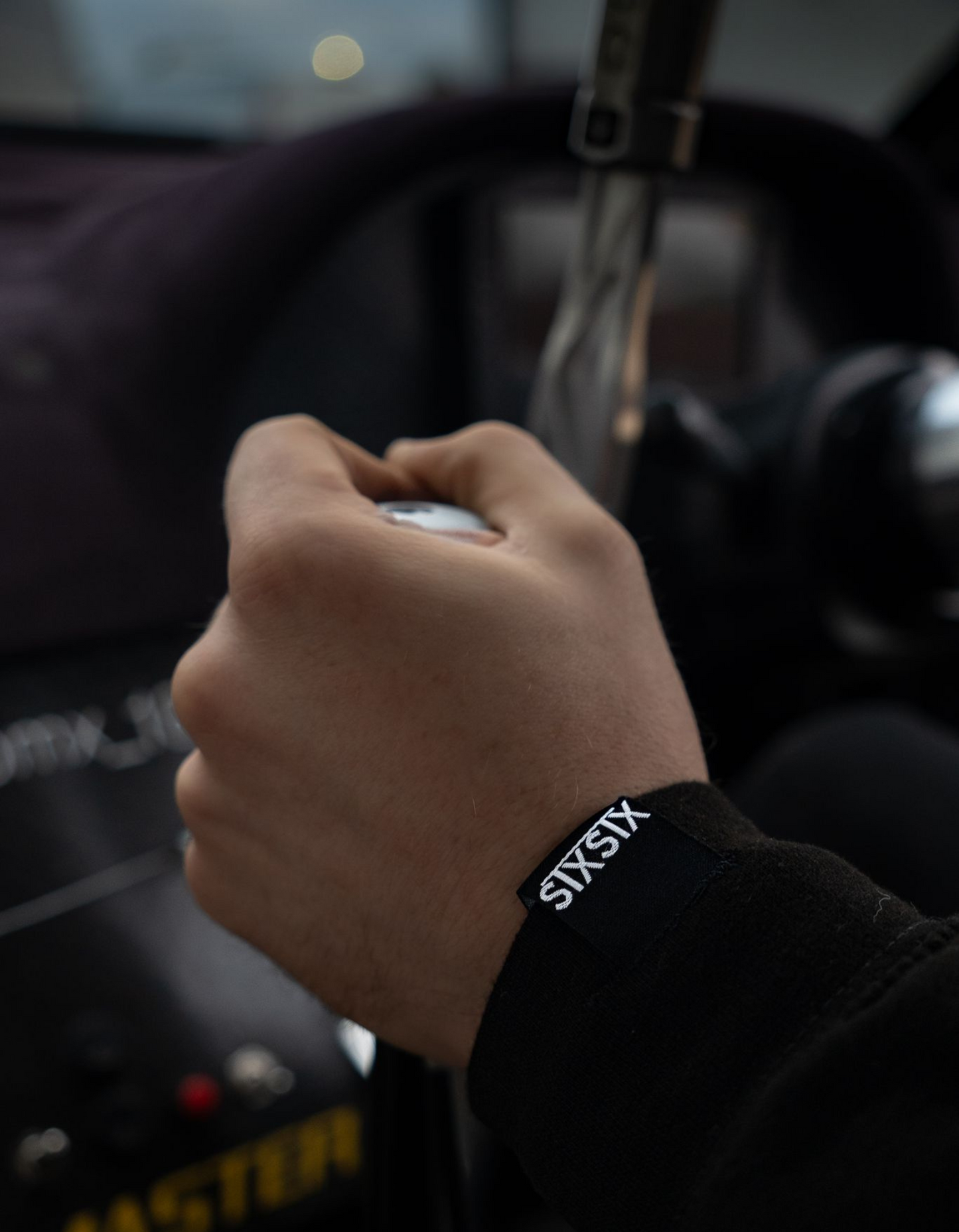 Hand gripping a gear knob showing the hem tag on a hoodie sleeve inside a vehicle.
