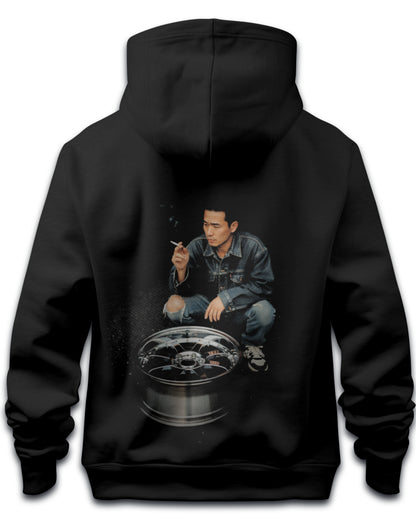 Black hoodie with a graphic of a japanese drifter person crouched over an alloy wheel expressing japanese drift culture on the back, on a white background