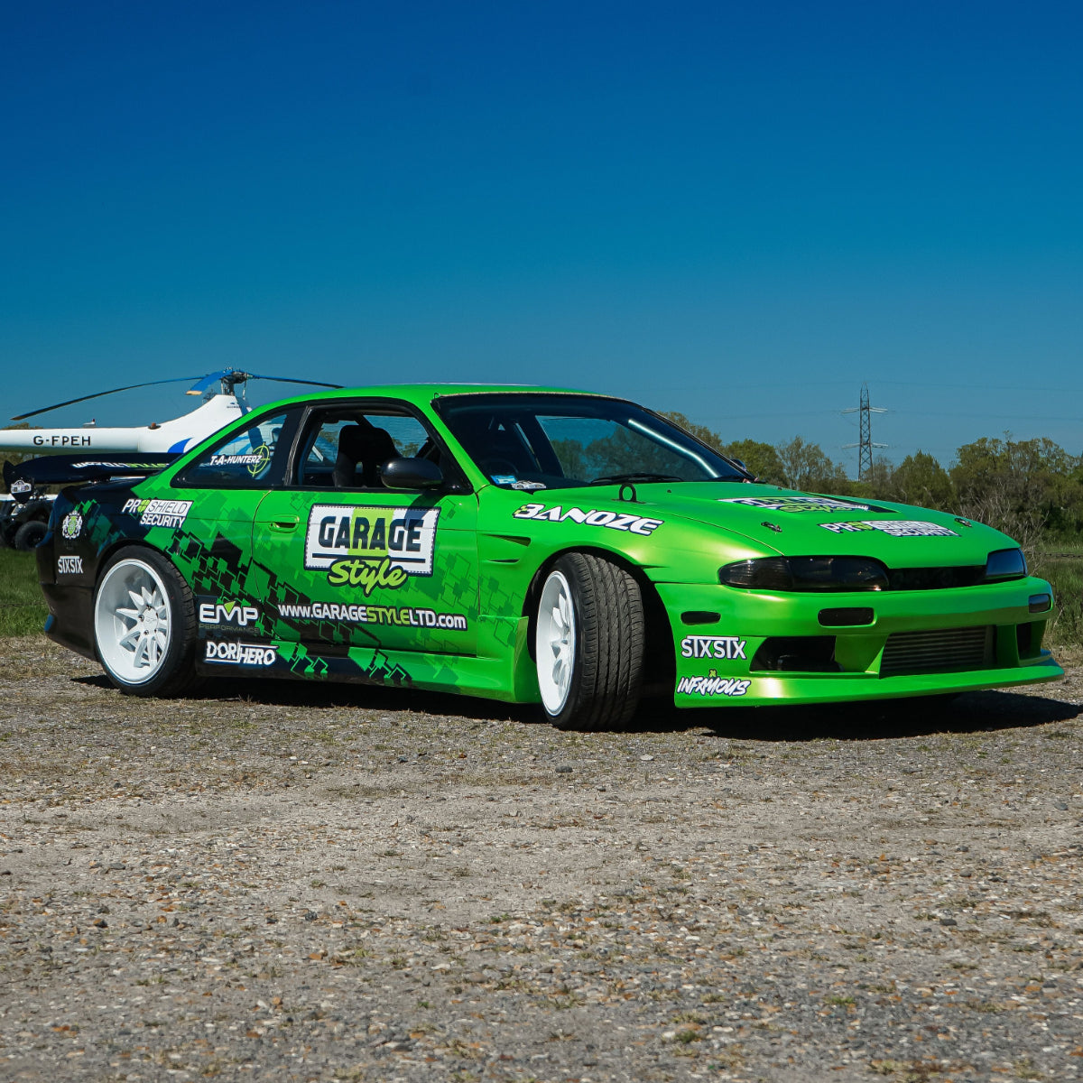 Green nissan s14 drift car with various sponsor logos on a gravel surface under a clear blue sky. - stxstx - danny grundy - premium