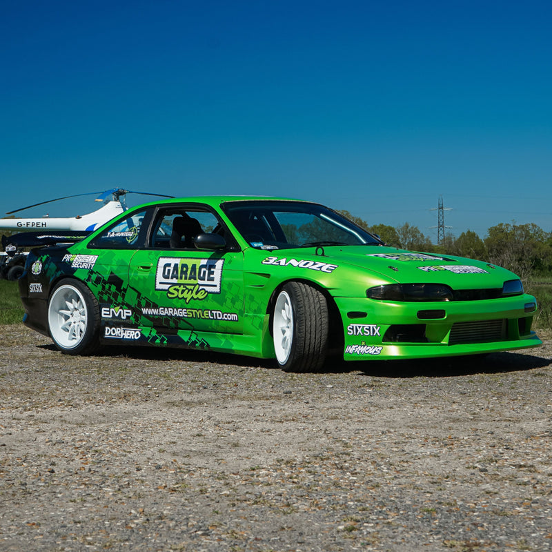 Green nissan s14 drift car with various sponsor logos on a gravel surface under a clear blue sky. - stxstx - danny grundy - premium