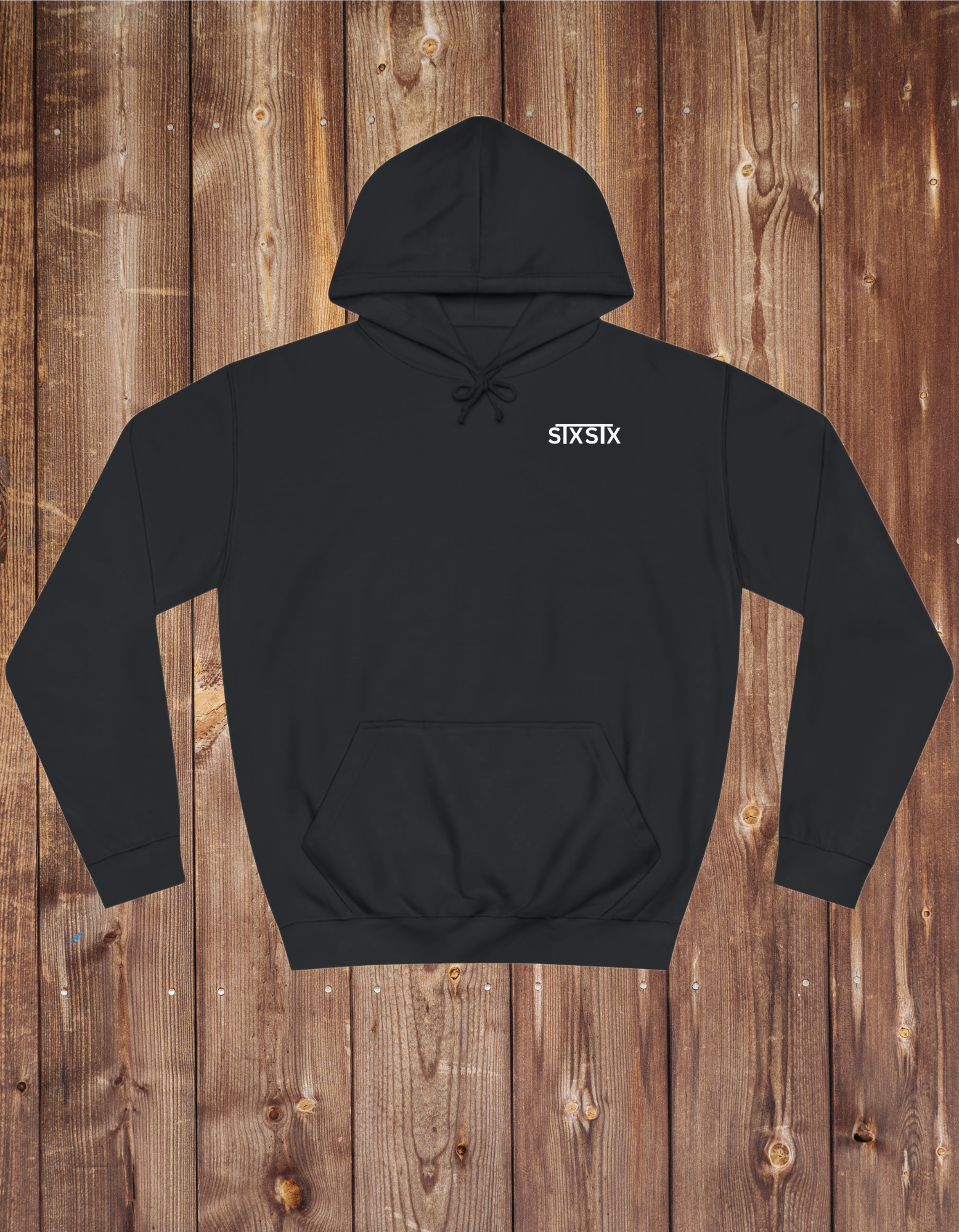 A black unisex hoodie with a double fabric hood, drop shoulder style, and front pouch pocket, displayed on a wooden background.