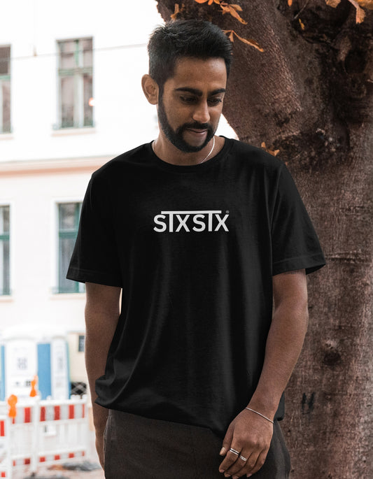 Man wearing a black t-shirt with 'STXSTX' logo standing next to a tree.