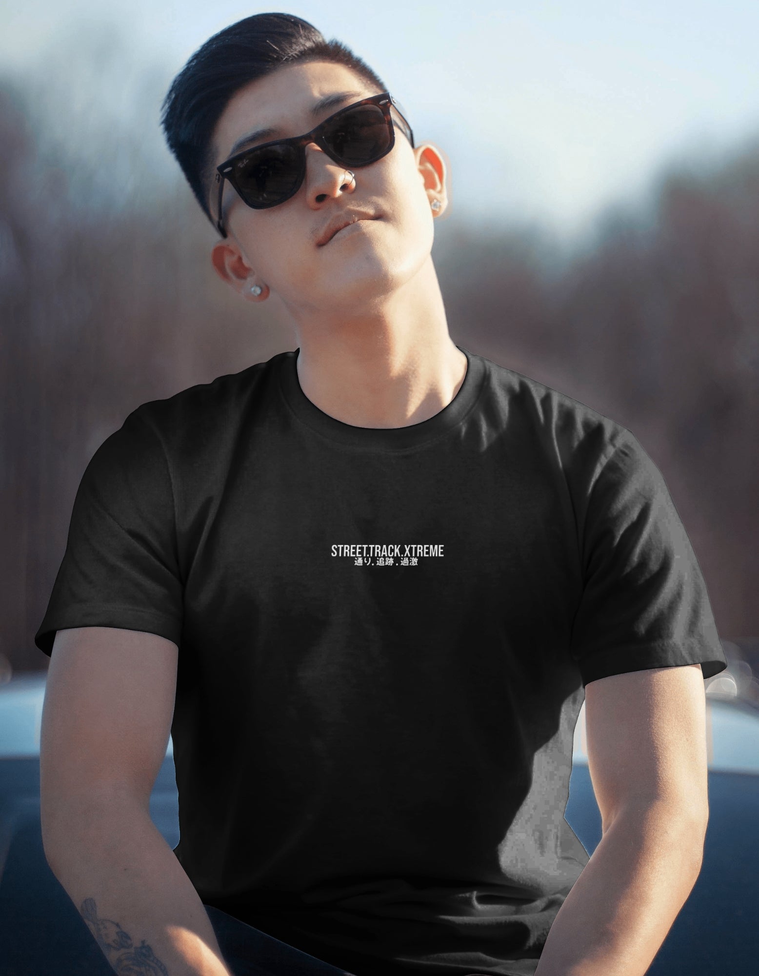Person wearing a black t-shirt with text, sitting outdoors. Text says: Street Track Xtreme
