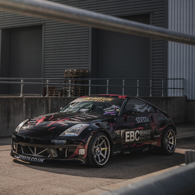 Black race car with various sponsor logos parked in front of a building.