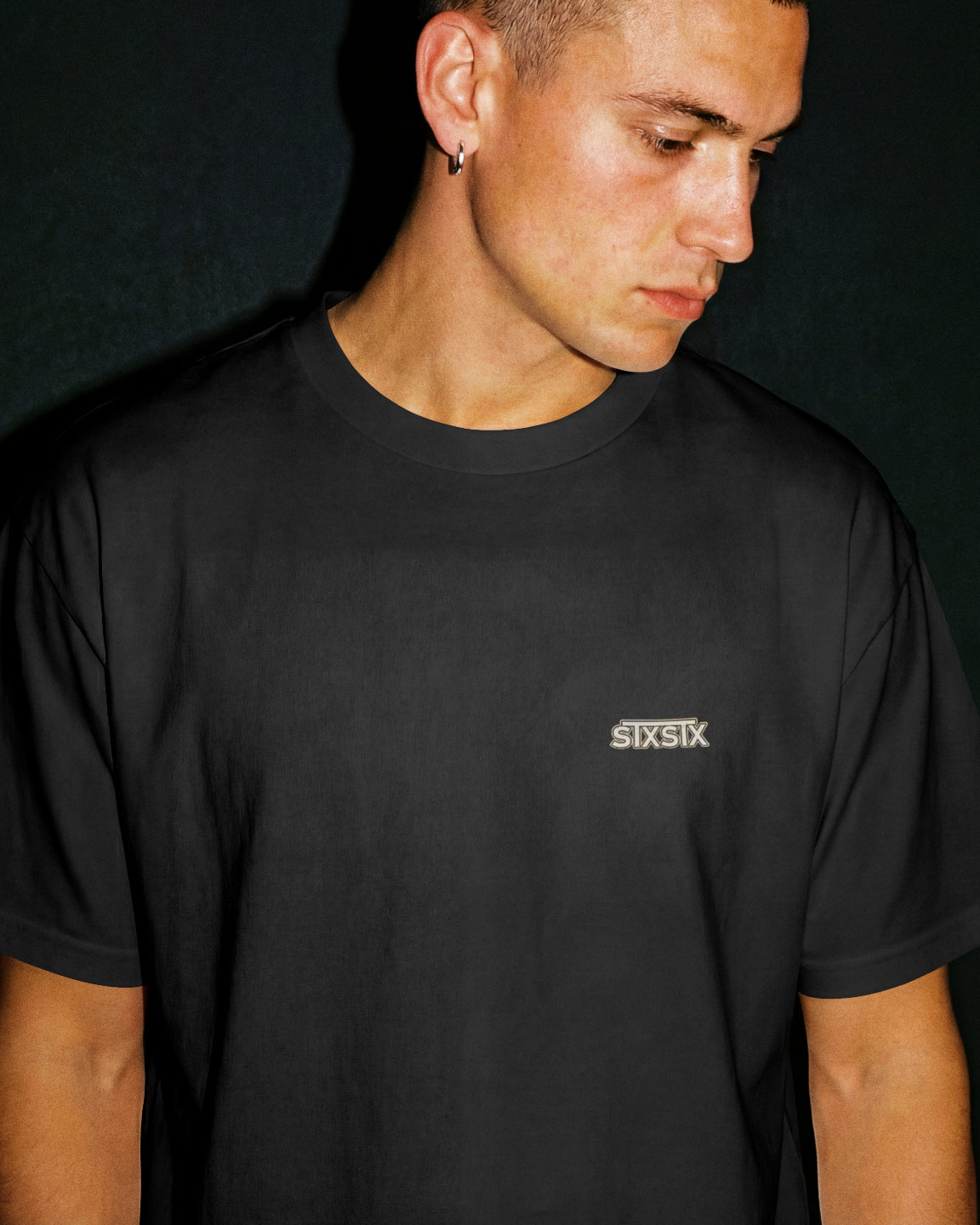 front shot of person wearing a premium black tshirt with small stxstx logo to the left chest. black background