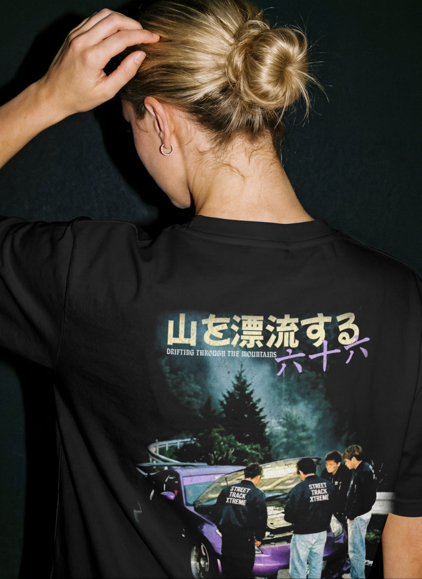model wearing black premium tshirt with a design of a nissan 350z parked up in the mountains with mates admiraring the work