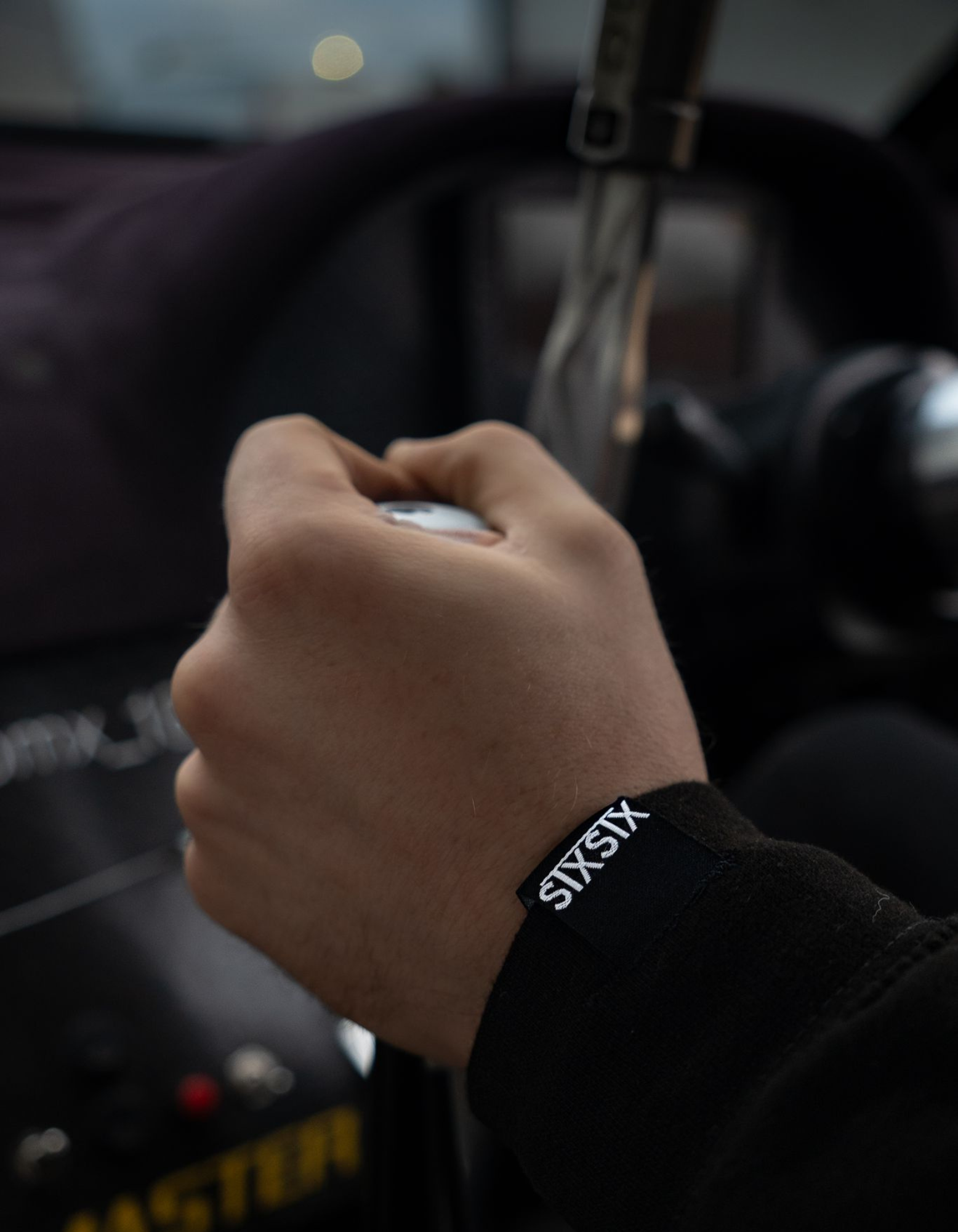 Hand gripping a gear knob showing the hem tag on the premium stxstx black hoodie sleeve inside a vehicle.