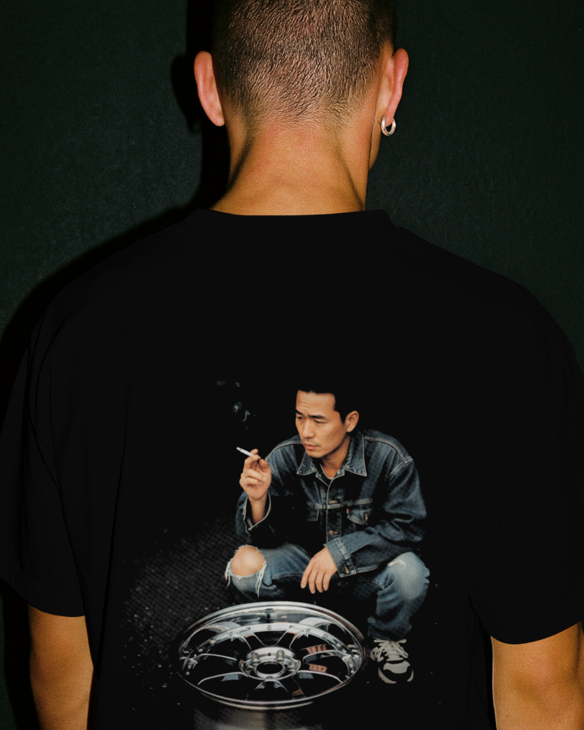 Black premium tshirt with a graphic of a japanese drifter person crouched over an alloy wheel expressing japanese drift culture on the back, on a black background